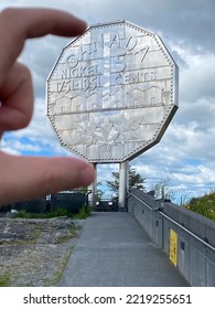Sudbury, Ontario, Canada -2022: Big Nickel - Giant Replica Of A 1951 Canadian Nickel At Dynamic Earth Science Museum. Fingers Grabbing Coin. 