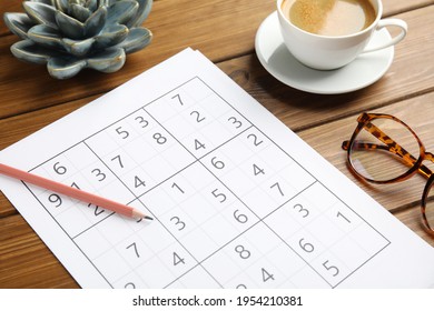 Sudoku, pencil, eyeglasses and cup of coffee on wooden table