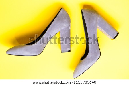 Suede footwear concept. Shoes made out of grey suede on yellow background. Footwear for women with thick high heels, top view. Pair of fashionable high heeled shoes.