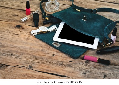 Suede Womens Bag With Tablet Computer, Watch And Women Cosmetics (lip Gloss, Mascara, Nail Polish And Spirits)  On A Wooden Table Closeup. Top View