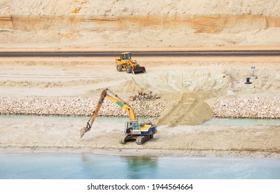 Suez Canal Construction Site. Backhoe And Frontend Loader Working In The Sandy Bank. View From The Water, Suez Canal, Egypt