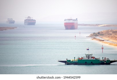 Suez Canal Zone. Ship Convoy In The Distant Desert Haze. A Local Ferry Between The East And West Bank In Foreground.