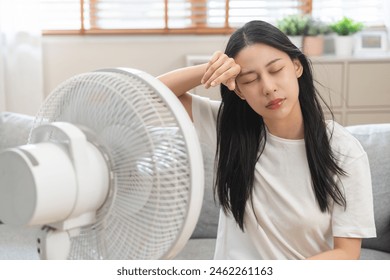 Suffer summer heat wave stroke, hot weather, tired asian young woman sitting on couch in living room without air-conditioner, using electric fan, wave fan to cool for ventilation when high temperature - Powered by Shutterstock