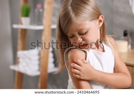 Suffering from allergy. Little girl scratching her arm in bathroom, space for text