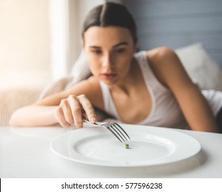 Suffering From Anorexia. Girl Is Trying To Put A Pea On The Fork