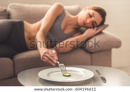 Suffering from anorexia. Slice of cucumber on the plate in the foreground, depressed girl lying in the background Imagine de stoc © 
