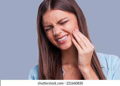 Suffering from toothache. Beautiful young woman suffering from toothache while standing against grey background
