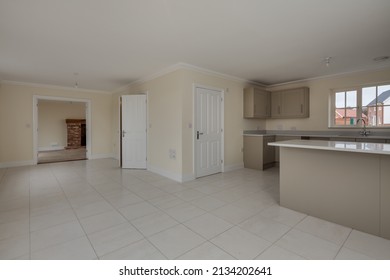 Suffolk, England - Feb 13 2018: Modern Empty Generic Kitchen And Family Room Within Brand New Vacant Home With Fitted Cabinets, Breakfast Bar, Ceramic Tiled Flooring And Door Open To Living Room.