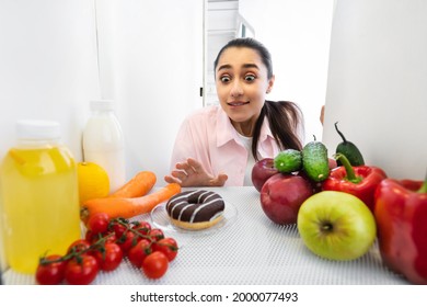 Sugar Addiction Concept. Portrait Of Funny Young Lady Reaching And Trying To Grab Yummy Doughnut Pie, View From Inside The Refrigerator. Sneaky Female On A Diet At Midnight