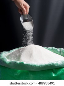 Sugar being poured from scoop into bag of sugar on dark background