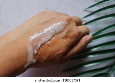 Sugar Coconut Skin Scrub Cream On Hand With Natural Tree Leaf On Table