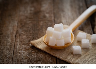 Sugar Cube In Wooden Spoon On Jute Napkin Over Wooden Background.