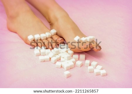 Sugar cubes lying in a row on female feet on pink background with copy space, depilation concept