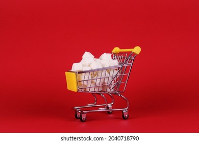 Sugar cubes in a miniature shopping trolley on a red background. High calorie food symbol
