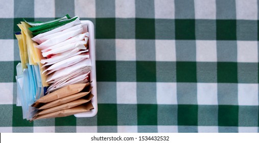 Sugar Packets On A Checkered White And Green Table Cloth