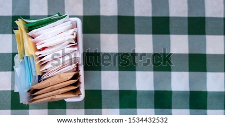 sugar packets on a Checkered white and green table cloth