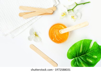 Sugar Paste Or Wax Honey In A Transparent Jar On A White Background. Sugaring. Depilation And Beauty Concept. Waxing. Beautiful Background With White Orchids. Relax Mood.