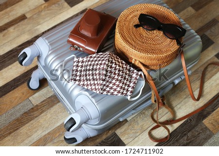 Suitcase with cloth cotton face mask on wooden floor background. Preparing for trip abroad after corona virus pandemic. Travel concept.