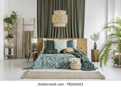 Suitcase And Hat On King-size Bed Against An Olive Cloth In Bedroom With Ladder And Rattan Lamp