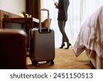 Suitcase in hotel room with businesswoman in the background. Copy space.