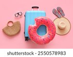 Suitcase with inflatable ring and beach accessories on pink background