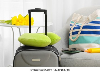 Suitcase And Neck Pillow Near Armchair With Traveler Accessories In Light Room