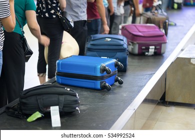 Suitcase on luggage conveyor belt at baggage claim at airport. Lines of people waiting for their baggage - Shutterstock ID 534992524