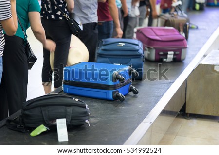 Suitcase on luggage conveyor belt at baggage claim at airport. Lines of people waiting for their baggage