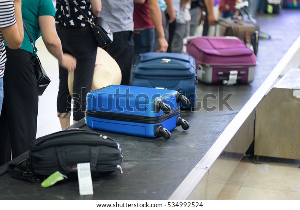 Suitcase on luggage\
conveyor belt at baggage claim at airport. Lines of people waiting\
for their baggage