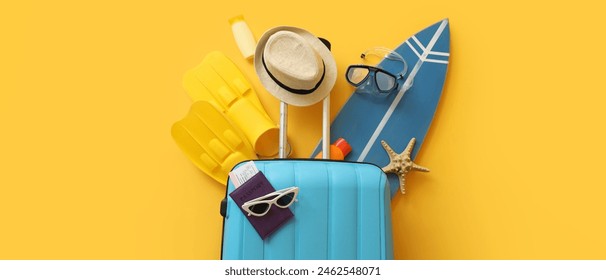 Suitcase with surfboard, passport and beach accessories on yellow background