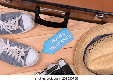 Suitcase and tourist stuff with inscription travel insurance on wooden background top view