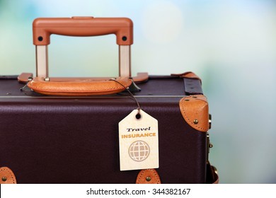 Suitcase With TRAVEL INSURANCE Label On Light Blurred Background