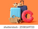 Suitcases with inflatable ring and beach accessories on orange background