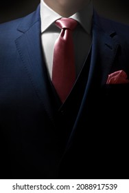 Suited businessman - mystery man close up dressed in an expensive formal suit. The jacket is navy blue with a matching waistcoat as well as a pink pocket square and tie.