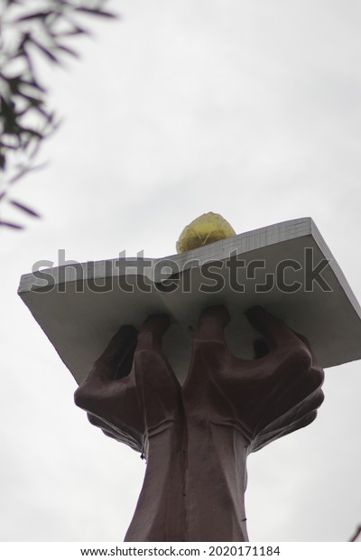 Sukabumi, West Java, Indonesia - September 22, 2020:\
Monument of a hand holding a book and a lotus in Sukabumi town\
square on a cloudy\
day.