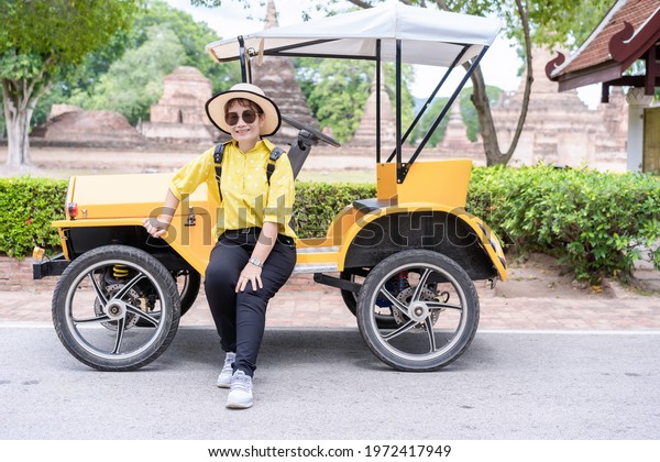 Sukhothai, Thailand-October 20, 2020: An\
unidentified woman sitting on old-style car use as shuttle vehicles\
for tourists to the ancient ruins of temple at Sukhotai Historical\
Park in Thailand