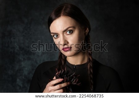 A sullen woman with pigtails is holding a black dahlia flower. Gothic style on a dark background