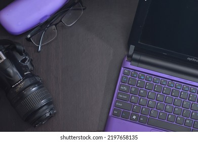 SUMBAWA BARAT, INDONESIA, 4th September 2022: Wooden Textured Workbench With Axioo Netbook, Nikon Camera And Anti Uv Glasses.  This Image Is Suitable As Wallpaper Or Design Background.