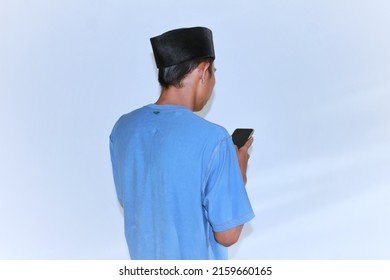 Sumenep Madura Indonesia 23 May 2022, Rear View Of Young Asian Man Wearing Bright Blue T-shirt Looking At Phone Screen. Isolated On White.