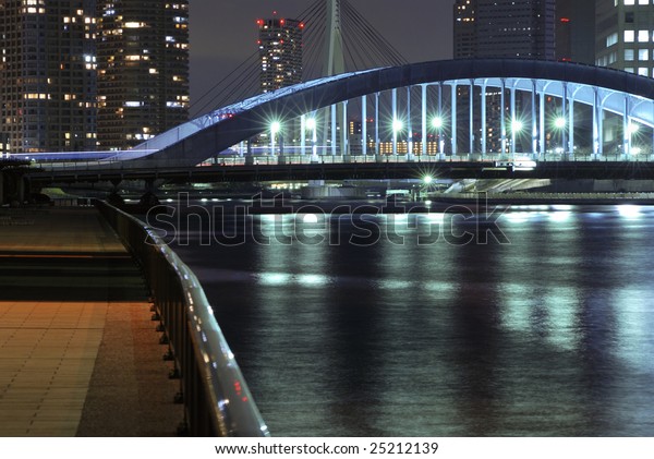 Sumida river embankment in central\
Tokyo by night with metallic Eitai bridge\
background