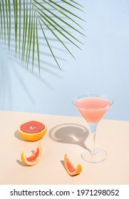 Summer 2021 Minimal Concept With Cocktail Glass, Pink Grapefruit Half And Peel And Palm Tree Leaf. Minimal Trendy Seasonal Design