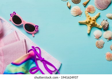 Summer Accessories Concept On Blue Background. Flatlay, Copyspace, Pink Sunglasses,  Colorful  Swimsuit, Hat And Towel. Seashells, Starfish. Summer Kids Clothes. Place For Text.