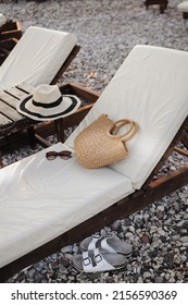 Summer accessories: straw hat, summer knitted bag, and sunglasses on a sunbed on the pebble beach. 