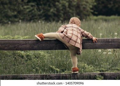 Summer adventures. Little girl climbs over the fence in the garden - Powered by Shutterstock