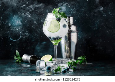 Summer alcoholic cocktail blueberry mojito with rum, mint, lime and ice, bar tools, gray background, selective focus