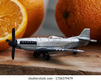 Summer Is Already Here, But Trips Is Still So Far Away.  Little Grey Toy Plane On The Wooden Olive Board With Tropical Oranges Around It. Close Up Of Grey Plane And Oranges.