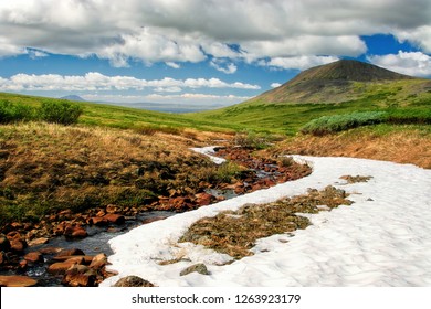 Summer In The Arctic. End Of June In The Far North. Beautiful Northern Nature. Chukotka Landscape. Snow And Tundra In The Valley Among The Hills In The Foothills Of The Golden Ridge. Chukotka, Russia.