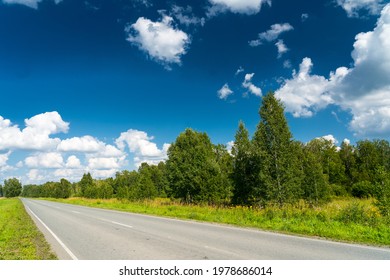 summer asphalt countryside road through young birch forest, bright blue sky and clouds, summertime sunny day landscape