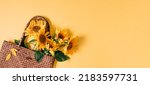 Summer or autumn background. Wicker bag with bouquet of sunflower flowers on yellow background. Flat lay, top view, copy space