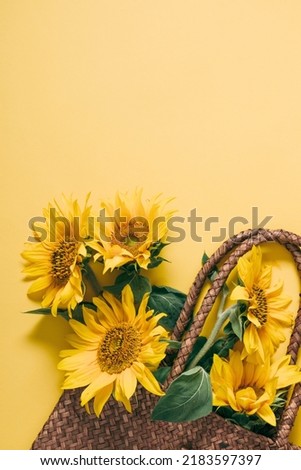 Summer or autumn background. Wicker bag with bouquet of sunflower flowers on yellow background. Flat lay, top view, copy space